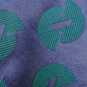 May include: Close-up of a patterned fabric with a repeating design. The background is a deep blue, with a textured appearance. The pattern consists of teal-colored, stylized letter "H" shapes, each filled with vertical stripes.