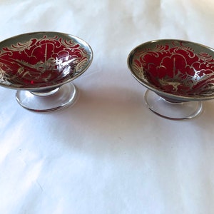 Puede incluir: Dos pequeños cuencos de vidrio rojo con diseños grabados en plata. Los cuencos tienen una base de pedestal.