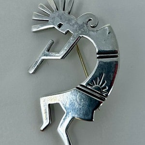 Puede incluir: Un broche de Kokopelli de plata con un diseño de sol. El broche está hecho de plata de ley y es un diseño tradicional nativo americano.