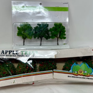 May include: A pack of five miniature apple trees for model railway layouts. The trees are green with red apples and are packaged in a clear plastic box. The box has the text "5 Apple Trees" and "Bachmann Scenic Products" printed on it.