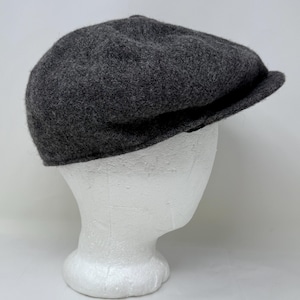 May include: A dark gray, wool newsboy cap with a rounded crown and a small, stiff brim. The hat is displayed on a white mannequin head, showcasing its shape and texture. The cap is a classic style, suitable for various outfits.