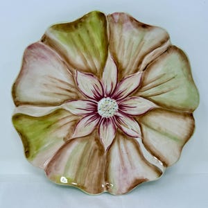 以下が含まれることがあります： 花型の装飾用セラミックプレート。 プレートの中央には白い中心とマルーンのアクセントが付いた花があります。 花びらは、淡い緑色、茶色、クリーム色の色が混ざり合っており、自然な外観を作り出しています。