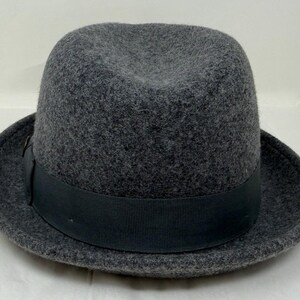 Pode incluir: Um chap&eacute;u fedora de feltro cinza-carv&atilde;o com uma copa estruturada com um vinco central e uma frente pin&ccedil;ada. O chap&eacute;u &eacute; circundado por uma faixa de fita gorgor&atilde;o preta s&oacute;lida que fica rente &agrave; base da copa acima da aba do chap&eacute;u.