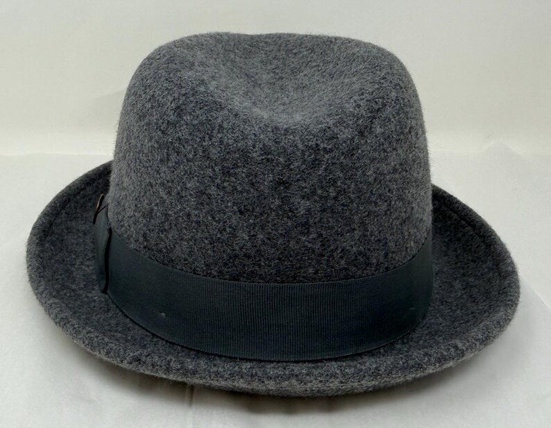 Pode incluir: Um chap&eacute;u fedora de feltro cinza-carv&atilde;o com uma copa estruturada com um vinco central e uma frente pin&ccedil;ada. O chap&eacute;u &eacute; circundado por uma faixa de fita gorgor&atilde;o preta s&oacute;lida que fica rente &agrave; base da copa acima da aba do chap&eacute;u.