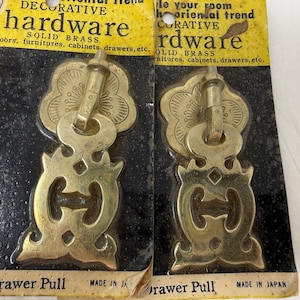 May include: Two decorative solid brass drawer pulls with an oriental design. Each pull has a floral top, a key-shaped center, and an ornate bottom. The packaging reads "Decorative Hardware" and "Made in Japan."