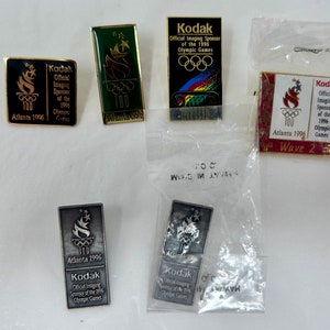 Puede incluir: Una colección de pines Kodak vintage de los Juegos Olímpicos de Atlanta 1996. Los pines presentan los anillos olímpicos, un diseño de antorcha y el logotipo de Kodak. Algunos están en su embalaje original.