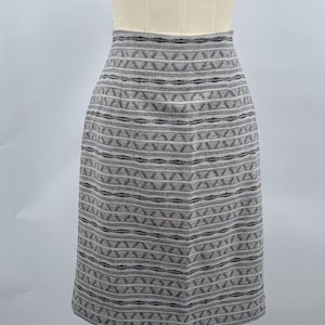 May include: A gray pencil skirt with a geometric pattern. The skirt is displayed on a mannequin. The pattern consists of horizontal stripes and zigzags in shades of gray and black. The skirt appears to be made of a woven fabric.