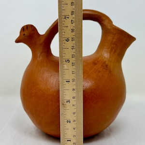 Könnte beinhalten: Eine terracotta-Keramikkanne in Form eines Huhns mit rundem Körper und Henkel. Die Kanne ist etwa 18 cm hoch.