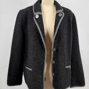 May include: A dark gray wool jacket with a gray trim and silver buttons. The jacket has a classic design with a notched collar, two front pockets, and a three-button closure. The jacket is displayed on a mannequin.