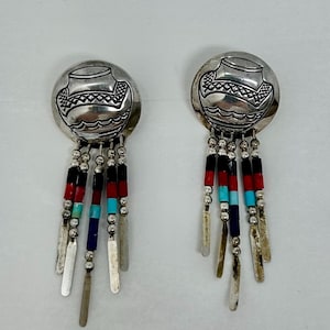 May include: A pair of silver earrings with a Native American pottery design. The earrings have a dangle design with silver beads and turquoise, red, and black stones.