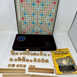 May include: A vintage Scrabble board game set with a black and brown box, wooden letter tiles, a game board with a star in the center, and a book titled "The Scrabble Word Guide".