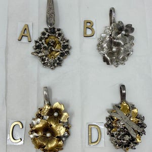 May include: Four ornate silver pendants with floral and nature-inspired designs. Each pendant features a decorative spoon handle. Designs include flowers, a fox, and a dragonfly. The pendants are displayed on a white surface.