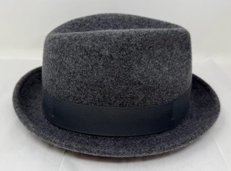 Pode incluir: Um chap&eacute;u fedora de feltro cinza-carv&atilde;o escuro com uma coroa estruturada com um vinco central e uma frente pin&ccedil;ada. O chap&eacute;u &eacute; acentuado com uma fita de gorgor&atilde;o preta lisa e s&oacute;lida que circunda a base da coroa acima da aba.