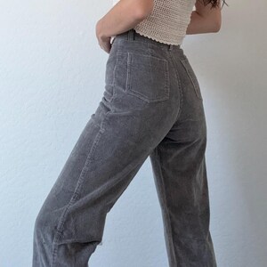 May include: A sleeveless, cream-colored crochet top paired with gray corduroy pants. The pants have a high waist and a straight leg. The outfit is casual and stylish, suitable for everyday wear.