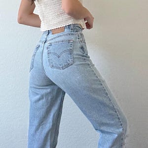 May include: A sleeveless, cream-colored crochet top paired with light-wash denim jeans. The jeans have a high waist and a classic five-pocket design. The outfit is simple and casual.
