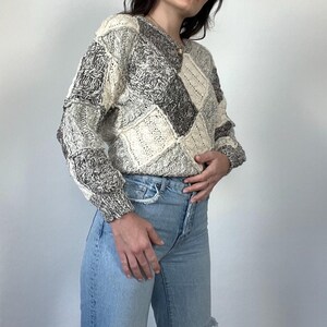 May include: A cream and gray patterned sweater with a loose fit and long sleeves. The sweater is made of a soft, knit fabric.