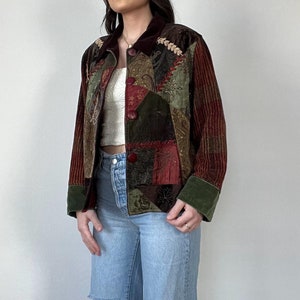May include: A patchwork corduroy jacket with a velvet collar and a button closure. The jacket is made up of different colored fabrics, including red, green, and brown. The jacket is worn over a white shirt and blue jeans.