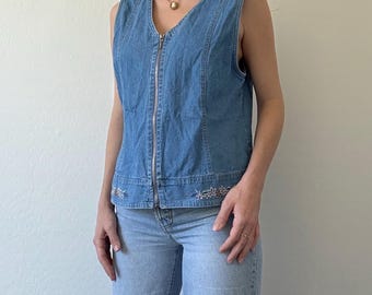 May include: A light blue denim vest with a zipper closure and silver embellishments. The vest has a V-neck and sleeveless design.