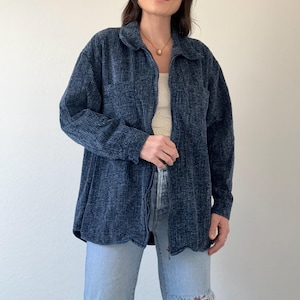 May include: A dark blue corduroy shirt with a collared neckline and long sleeves. The shirt has a button-up front and two chest pockets. The model is wearing light blue ripped jeans. The shirt is a casual, everyday garment.