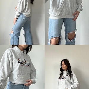 May include: A gray hooded sweatshirt with a Mickey Mouse graphic and the text "Mickey Mouse's Clubhouse" on the front. The sweatshirt is being worn by a person with long dark hair and blue jeans.