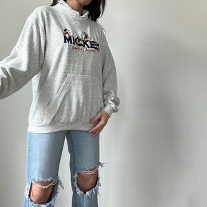 May include: A gray hooded sweatshirt with a Mickey Mouse graphic and the text "Mickey America's Favorite" embroidered on the front.