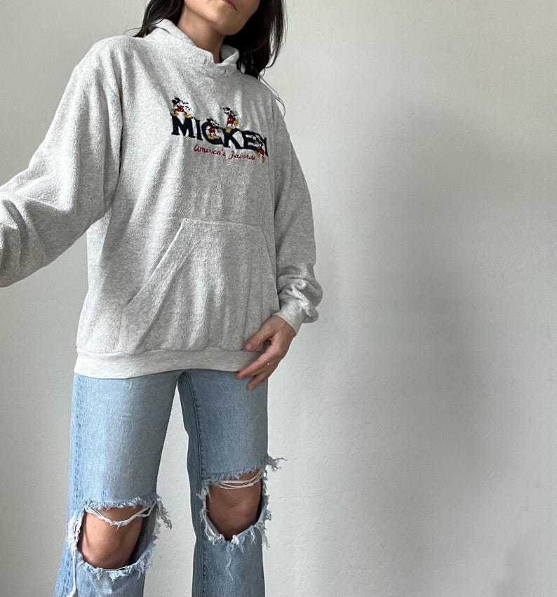 May include: A gray hooded sweatshirt with a Mickey Mouse graphic and the text "Mickey America's Favorite" embroidered on the front.