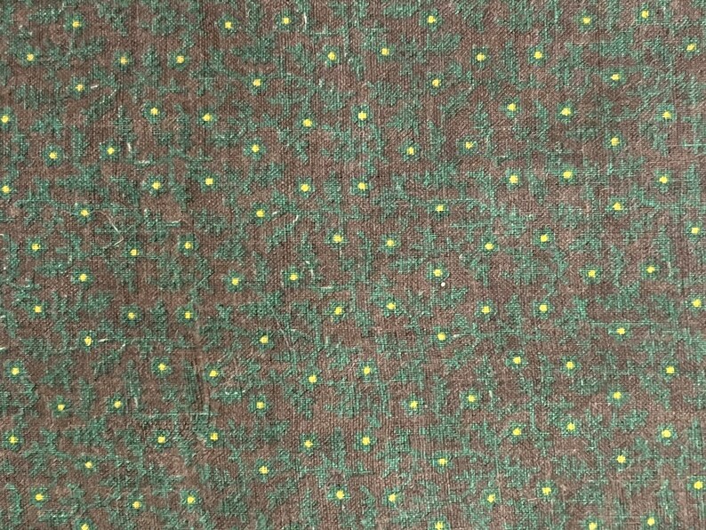 May include: Close-up of a fabric with a repeating pattern of small yellow dots and green floral shapes on a dark brown background. The fabric has a textured appearance.