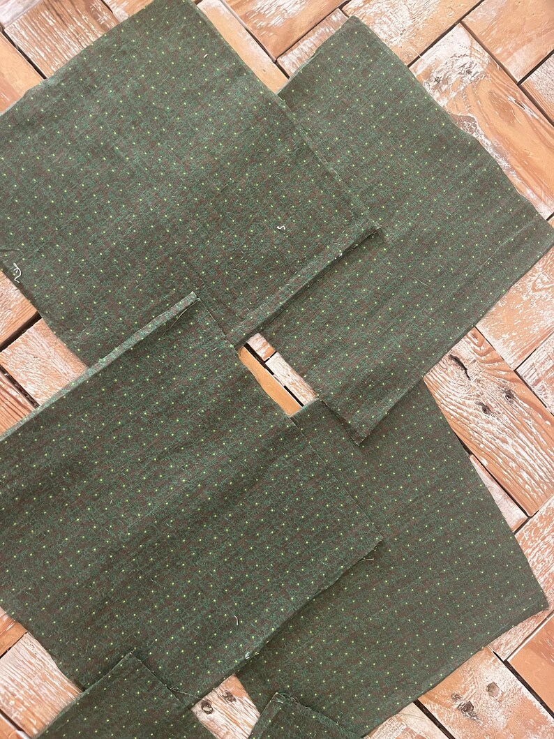 May include: A collection of six square, dark green fabric napkins with a subtle dotted pattern in a lighter green. The napkins are arranged on a light brown wooden surface, showcasing their texture and design. Ideal for home decor or dining.