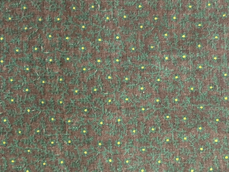 May include: Close-up of a fabric with a repeating pattern of small yellow dots and green floral shapes on a dark brown background. The fabric has a textured appearance.