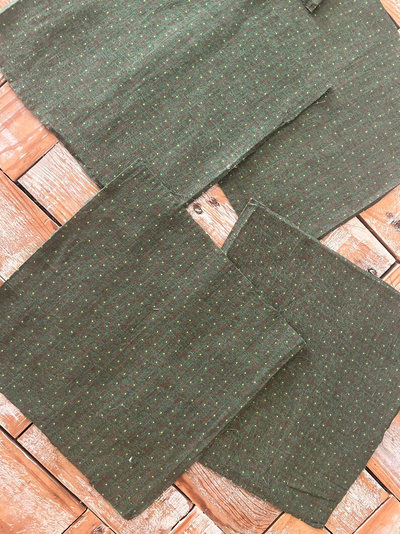 May include: Four dark green fabric napkins with a subtle dotted pattern in a lighter green. The napkins are arranged on a wooden surface, showcasing their texture and design. The fabric appears to be a woven material.