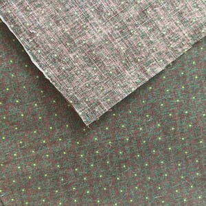 May include: Two pieces of fabric, one layered over the other. The bottom fabric is dark brown with a pattern of small green leaves and yellow dots. The top fabric is a lighter brown with a woven texture and small yellow dots.
