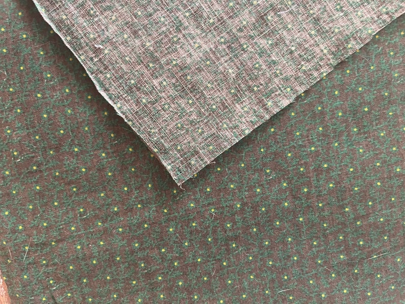 May include: Two pieces of fabric, one layered over the other. The bottom fabric is dark brown with a pattern of small green leaves and yellow dots. The top fabric is a lighter brown with a woven texture and small yellow dots.