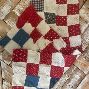 May include: A collection of patchwork quilt squares in various stages of completion. The squares feature red, white, and blue fabrics with patterns like polka dots, floral prints, and gingham. The unfinished edges and different fabric patterns suggest a handmade, vintage aesthetic.