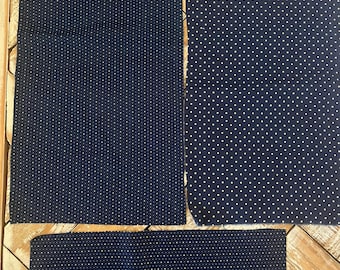 May include: Four pieces of navy blue fabric with a white polka dot pattern. The fabric pieces are rectangular and vary in size. The fabric is arranged on a wooden surface.