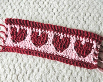 May include: A close-up of a crocheted trim with alternating rows of red and pink hearts.