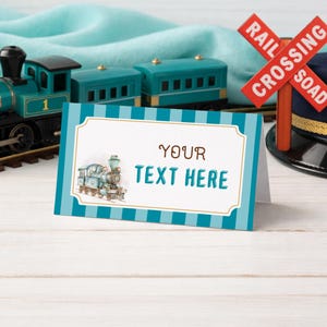 May include: A blue and white striped place card with the text "YOUR TEXT HERE" and a train illustration. A toy train and a railroad crossing sign are in the background. The train is teal and black.