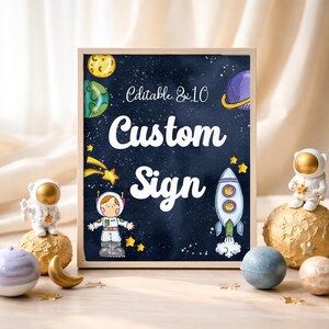 Peut inclure: Un panneau encadré avec un fond bleu foncé portant les mots "Custom Sign" en blanc. Le panneau présente des illustrations de planètes, d'étoiles, d'une fusée et d'un astronaute. Des figurines et des planètes décoratives sur le thème de l'espace entourent le panneau.