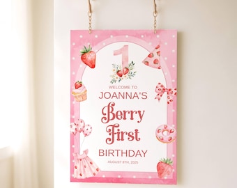May include: A pink sign with a strawberry theme, featuring the text "Joanna's Berry First Birthday" and the date August 8th, 2025. The sign includes illustrations of strawberries, a cupcake, a bow, and a donut.