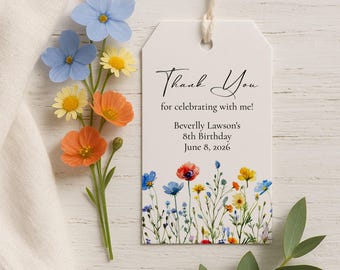 May include: A white gift tag with a floral border and the words "Thank You" in script. The tag includes the text "for celebrating with me!" and details for a birthday. A sprig of colorful flowers is next to the tag.