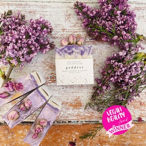 May include: Handmade soap bar with purple swirls and dried rosebuds, labelled "goddess". The soap is surrounded by purple lilac flowers and smaller soap bars. Includes a "Vegan Beauty Award Winner" sticker.