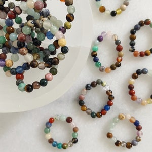 May include: A collection of colourful gemstone bracelets, each featuring a variety of stones in different shapes and sizes. The bracelets are arranged on a white surface.