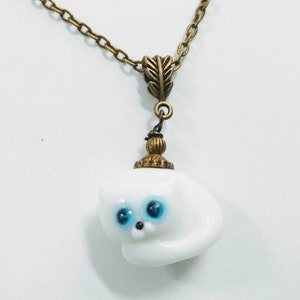 May include: A white porcelain cat charm with blue eyes, hanging from a bronze chain with a leaf-shaped clasp.