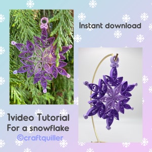 May include: A purple and white paper snowflake ornament with a gold hanger. The snowflake is on a gold stand and is surrounded by a white background with snowflakes. The text "Instant download" and "1 video tutorial for a snowflake @craftquiller" is visible in the image.