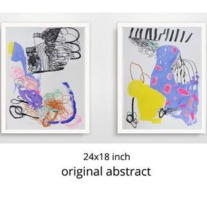 Op de afbeelding: Twee abstracte schilderijen in witte lijsten. Het schilderij aan de linkerkant heeft een mix van zwarte, blauwe, paarse, roze en gele verf. Het schilderij aan de rechterkant heeft een mix van zwarte, blauwe, gele, roze en witte verf. Beide schilderijen zijn 24x18 inch.
