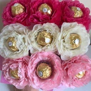 Puede incluir: Un ramo de flores de papel rosa, blanco y rosa claro con caramelos de chocolate en el centro de cada flor.