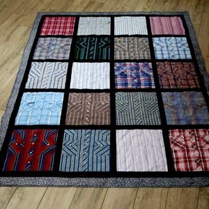 May include: A patchwork quilt made from various button-down shirts. The quilt features a grid pattern with each square showcasing a different shirt design, including plaids, stripes, and solid colors. The quilt is bordered with a dark gray fabric.