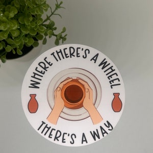 May include: A white round sticker with the text "Where there's a wheel there's a way" in black lettering. The sticker features a graphic of hands shaping clay on a pottery wheel.