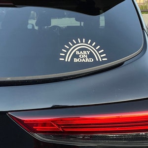 May include: A black car with a white sticker that says "Baby On Board" with a sun graphic above the text.