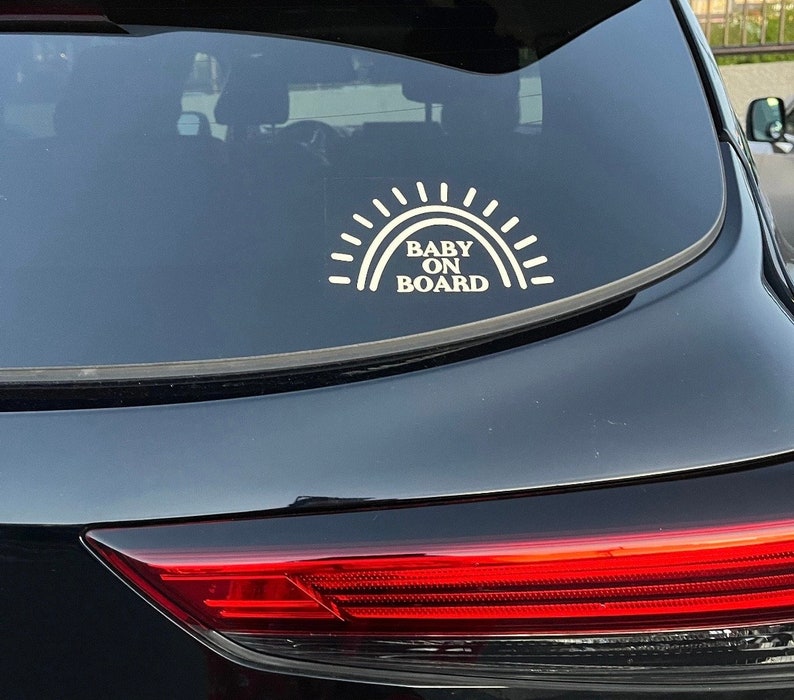 May include: A black car with a white sticker that says "Baby On Board" with a sun graphic above the text.