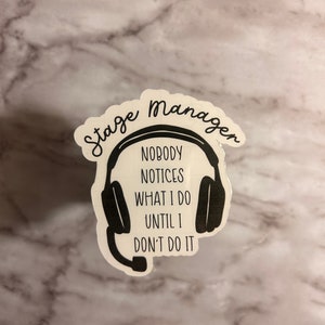 May include: Black and white sticker with a headset and the text "Stage Manager Nobody Notices What I Do Until I Don't Do It."